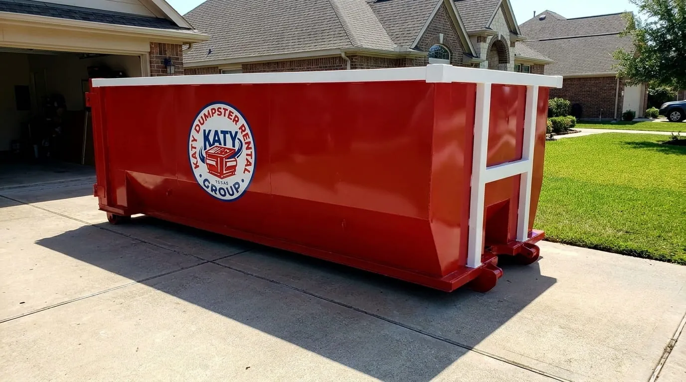 Red roll-off dumpster on a residential driveway beside a lawn in Katy, Texas Red roll-off dumpster on a residential driveway beside a lawn in Katy, Texas